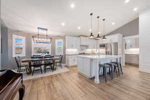 Kitchen featuring appliances with stainless steel finishes, a kitchen bar, an island with sink, light wood-type flooring, and recessed lighting