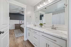 Full bath with double vanity, ceiling fan, wood finished floors, ensuite bathroom, and vaulted ceiling