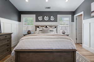 Bedroom with wainscoting, a decorative wall, multiple windows, wood finished floors, and recessed lighting