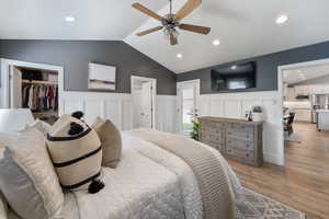 Bedroom featuring lofted ceiling, a wainscoted wall, stainless steel fridge, light wood-style floors, and recessed lighting