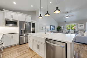 Kitchen featuring stainless steel appliances, vaulted ceiling, open floor plan, a sink, and light wood finished floors