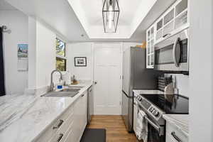 Kitchen featuring stainless steel appliances, a sink, light wood-style floors, white cabinetry, and glass insert cabinets