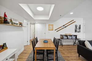 Dining area with light wood finished floors, baseboards, a tray ceiling, and recessed lighting