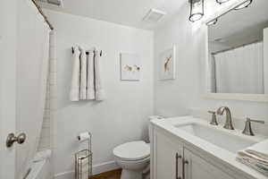 Full bath featuring vanity, toilet, wood finished floors, baseboards, and shower / bathtub combination with curtain