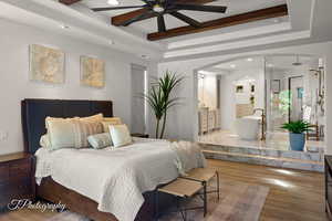 Bedroom featuring a raised ceiling, arched walkways, wood finished floors, recessed lighting, and ensuite bathroom