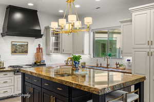 Kitchen with wall chimney exhaust hood, a sink, a kitchen island with sink, stainless steel gas cooktop, and recessed lighting