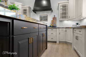 Kitchen featuring glass insert cabinets, white cabinetry, light wood-style flooring, and backsplash
