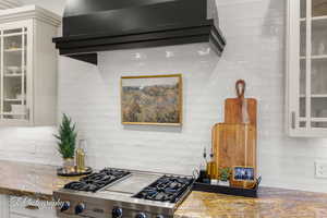 Kitchen featuring designer stove, tasteful backsplash, stone countertops, glass insert cabinets, and white cabinetry