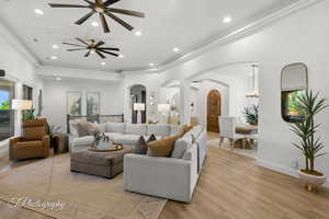 Living area featuring arched walkways, ceiling fan, light wood-style floors, ornamental molding, and recessed lighting