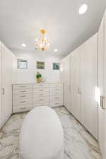 Spacious closet featuring light marble finish floors and a chandelier