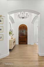 Foyer featuring a chandelier, light wood-style floors, arched walkways, and baseboards
