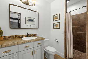 Full bath featuring vanity, toilet, a tile shower, and wood finished floors
