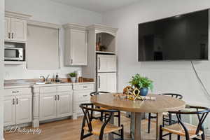 Kitchen featuring stainless steel microwave, a sink, light wood-type flooring, white cabinetry, and open shelves