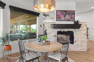 Dining room with ceiling fan, wood finished floors, a stone fireplace, ornamental molding, and baseboards