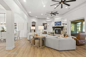Living room featuring arched walkways, ceiling fan, crown molding, a stone fireplace, and recessed lighting
