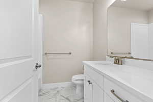 Bathroom featuring marble look tile flooring, vanity, toilet, and baseboards