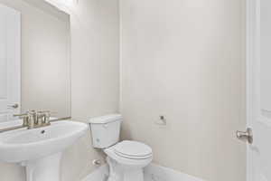 Half bath with baseboards, toilet, and a sink