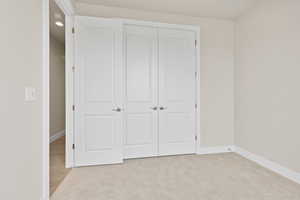 Unfurnished bedroom with baseboards, a closet, and light colored carpet