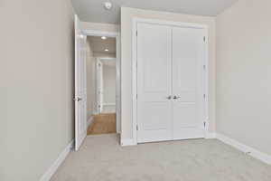 Unfurnished bedroom with light colored carpet, a closet, baseboards, and recessed lighting