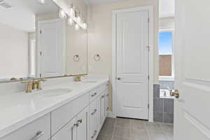 Bathroom with double vanity, tile patterned floors, and tiled bath