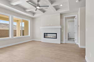 Unfurnished living room with coffered ceiling, a ceiling fan, light wood finished floors, a tile fireplace, and baseboards