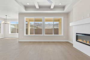 Unfurnished living room with wood finished floors, a mountain view, a tiled fireplace, a chandelier, and baseboards