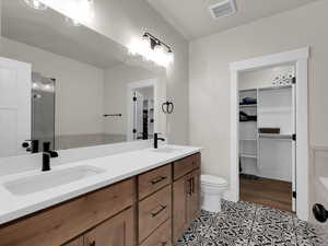 Full bath with double vanity, a walk in closet, toilet, a shower, and tile patterned flooring