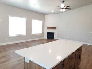 Kitchen with light countertops, open floor plan, light wood-style flooring, ceiling fan, and a large fireplace