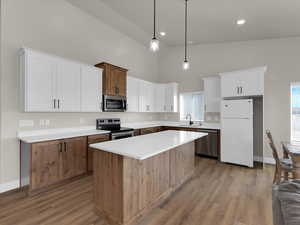 Kitchen featuring stainless steel appliances, a towering ceiling, a sink, light wood finished floors, and a center island