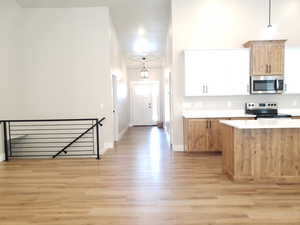 Kitchen with stainless steel appliances, light wood finished floors, light countertops, hanging light fixtures, and baseboards