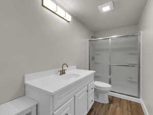Bathroom with a stall shower, wood finished floors, toilet, and vanity
