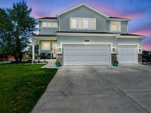 Traditional home featuring a garage, stucco siding, a front yard, driveway, and stone siding