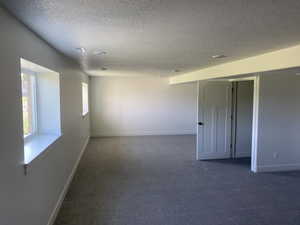Empty room with a textured ceiling, dark colored carpet, and baseboards