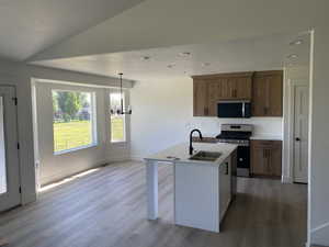 Kitchen with a sink, stainless steel appliances, light wood finished floors, a kitchen island with sink, and light countertops