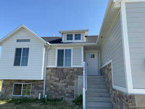 Entrance to property featuring stone siding and roof with shingles