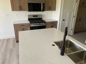 Kitchen featuring stainless steel gas range oven, a sink, baseboards, and light wood-style floors