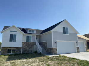View of front of property featuring stone siding, a garage, driveway, and roof with shingles