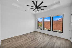 Spare room featuring wood finished floors, a raised ceiling, baseboards, a ceiling fan, and recessed lighting