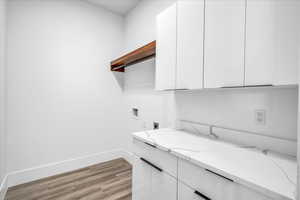 Laundry area featuring electric dryer hookup, hookup for a washing machine, light wood-type flooring, baseboards, and cabinet space