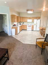 Kitchen with white appliances, light countertops, light brown cabinets, a sink, and light colored carpet