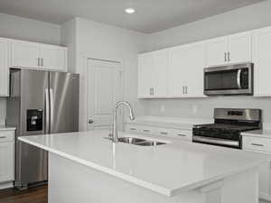 Kitchen featuring stainless steel appliances, a sink, dark wood-style floors, light countertops, and a kitchen island with sink