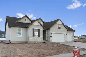 View of front of property with stone siding, stucco siding, driveway, and a shingled roof