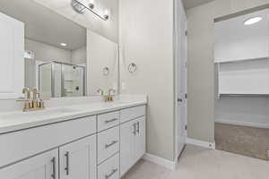 Full bathroom featuring double vanity, a shower stall, a walk in closet, baseboards, and tile patterned flooring