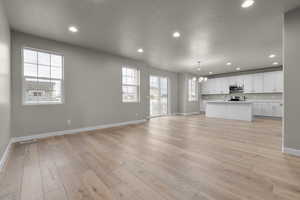Unfurnished living room with baseboards, a chandelier, a sink, light wood-type flooring, and recessed lighting