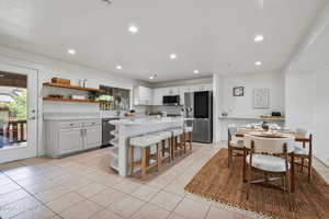 Kitchen featuring stainless steel appliances, light countertops, light tile patterned floors, a breakfast bar, and open shelves