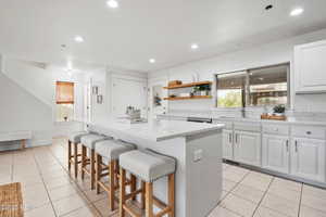 Kitchen featuring a kitchen island, light tile patterned flooring, white cabinetry, a kitchen breakfast bar, and open shelves