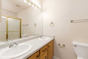 Primary en-suite bathroom featuring toilet, double vanity, a shower with shower door, and baseboards