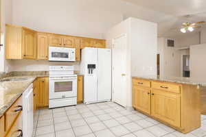 Kitchen featuring white appliances, a sink, a peninsula, ceiling fan, and lofted ceiling, granite countertops