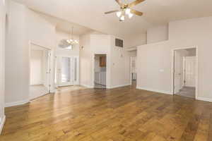 Unfurnished living room featuring hardwood / wood-style flooring, ceiling fan, a chandelier, high vaulted ceiling, and baseboards