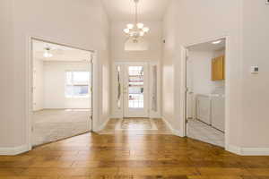 Entrance foyer with light wood-type flooring, washer and clothes dryer, a chandelier, a high ceiling, and baseboards